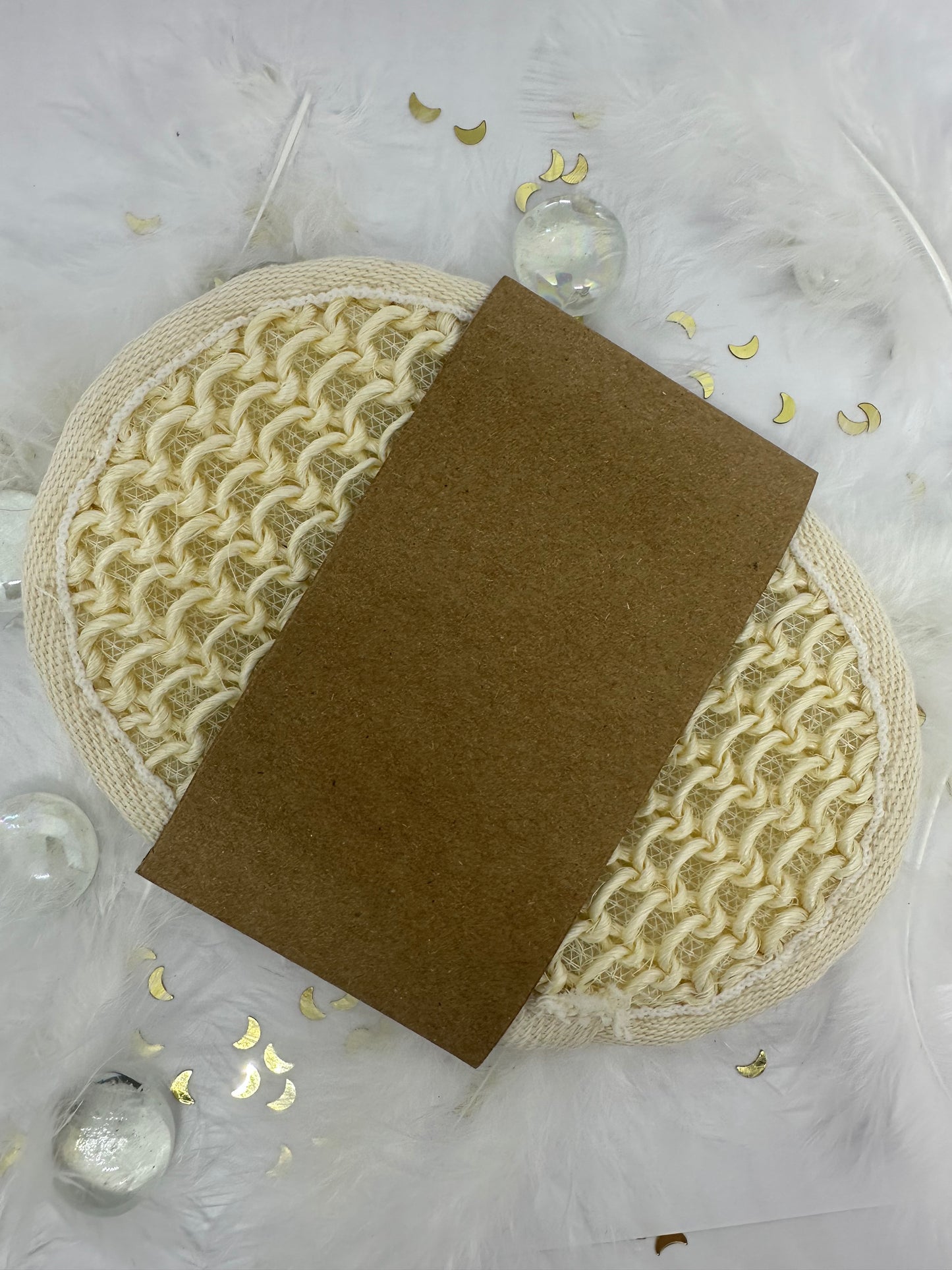 éponge exfolliante écru en coton sur fond blanc avec paillettes dorées, plumes blanches et billes transparentes
