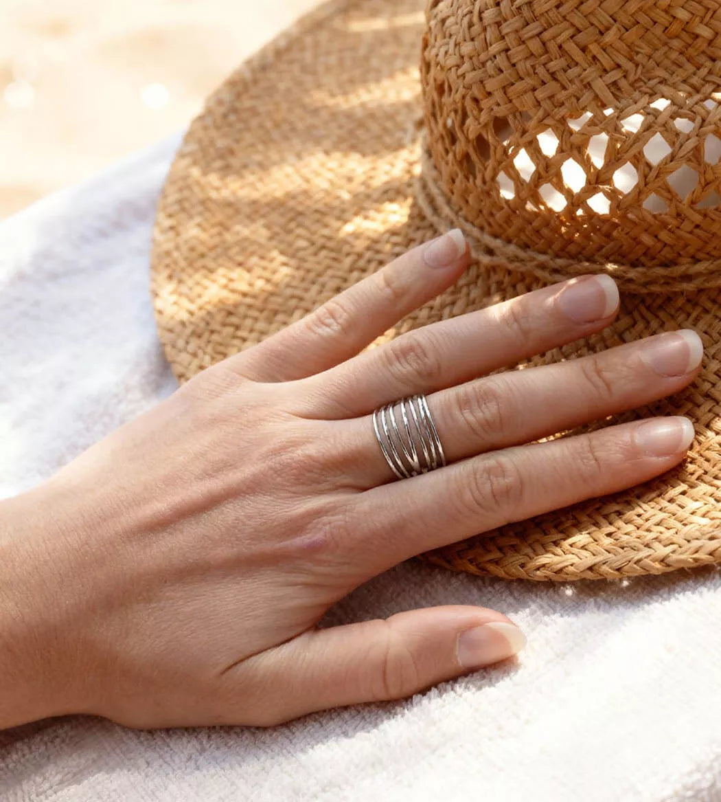 Bague kyma argent à filaments sur main femme posée sur un chapeau
