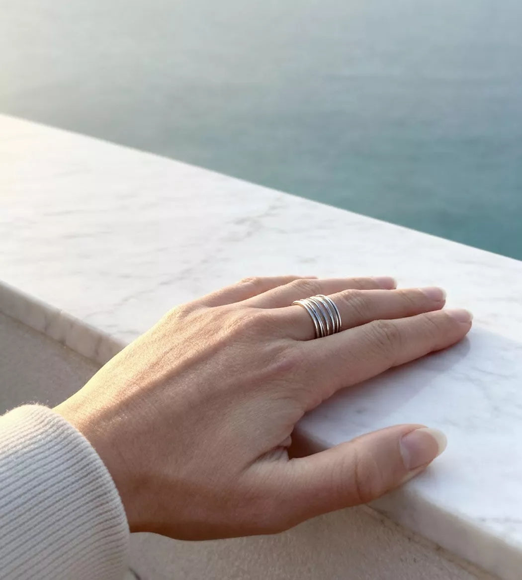 Bague kyma argent à filaments sur main posée sur rebord en marbre face mer