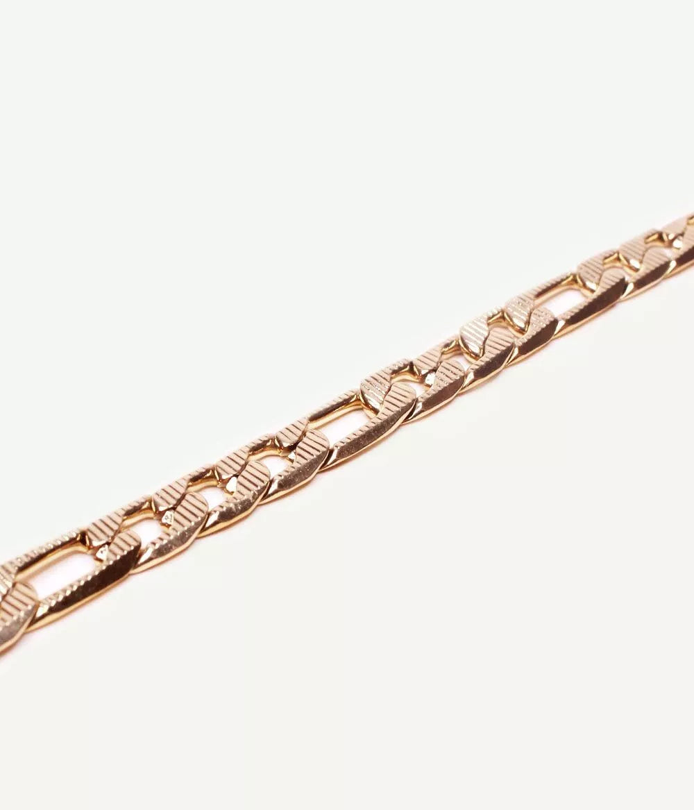 gros plan sur bracelet doré maille figaro sur fond blanc