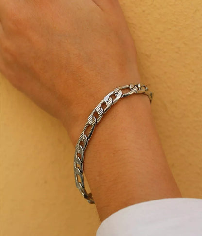 bracelet argenté maille figaro sur poignet femme femme quipose sa main sur le mur