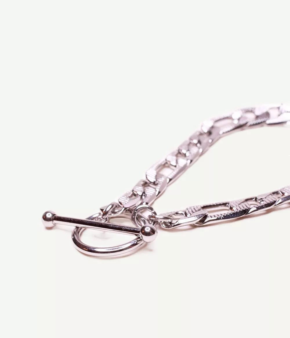 gros plan sur attache tige dans un cercle du bracelet argenté maille figaro sur fond blanc 