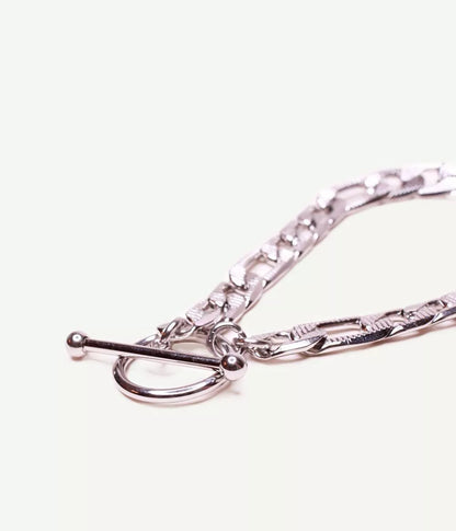gros plan sur attache tige dans un cercle du bracelet argenté maille figaro sur fond blanc 