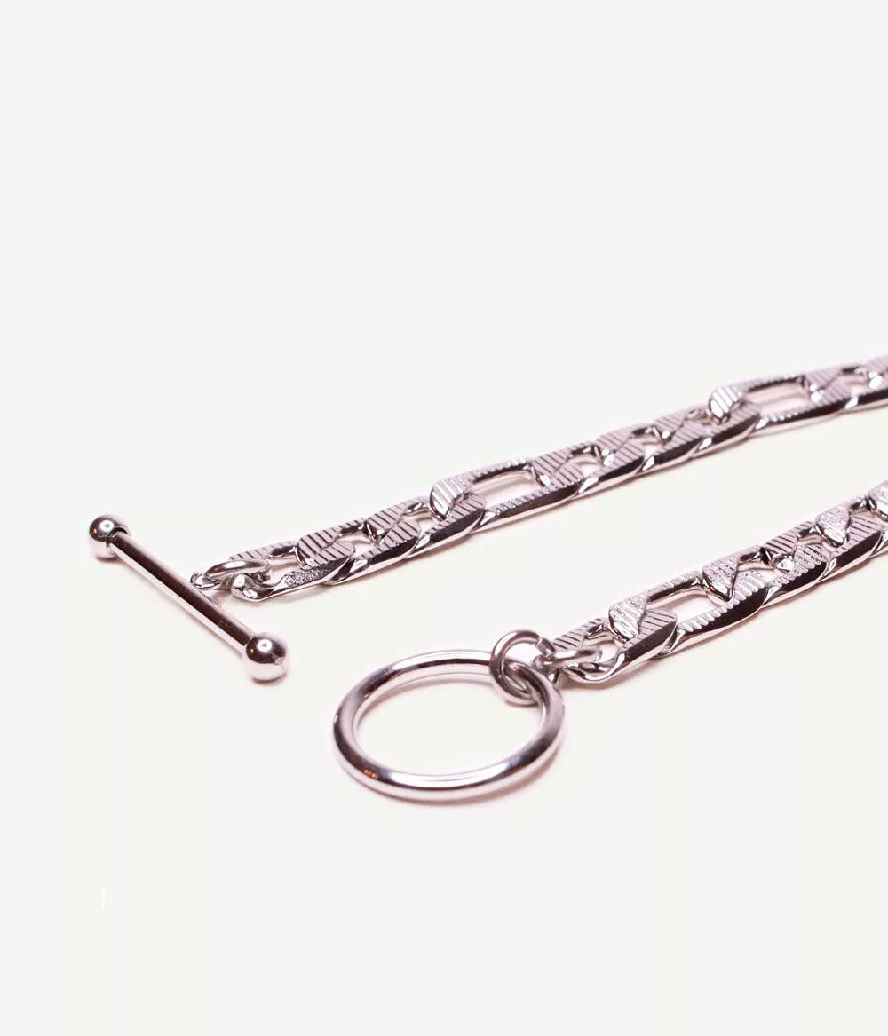 gros plan sur attache tige dans un cercle ouvert du bracelet argenté maille figaro sur fond blanc 
