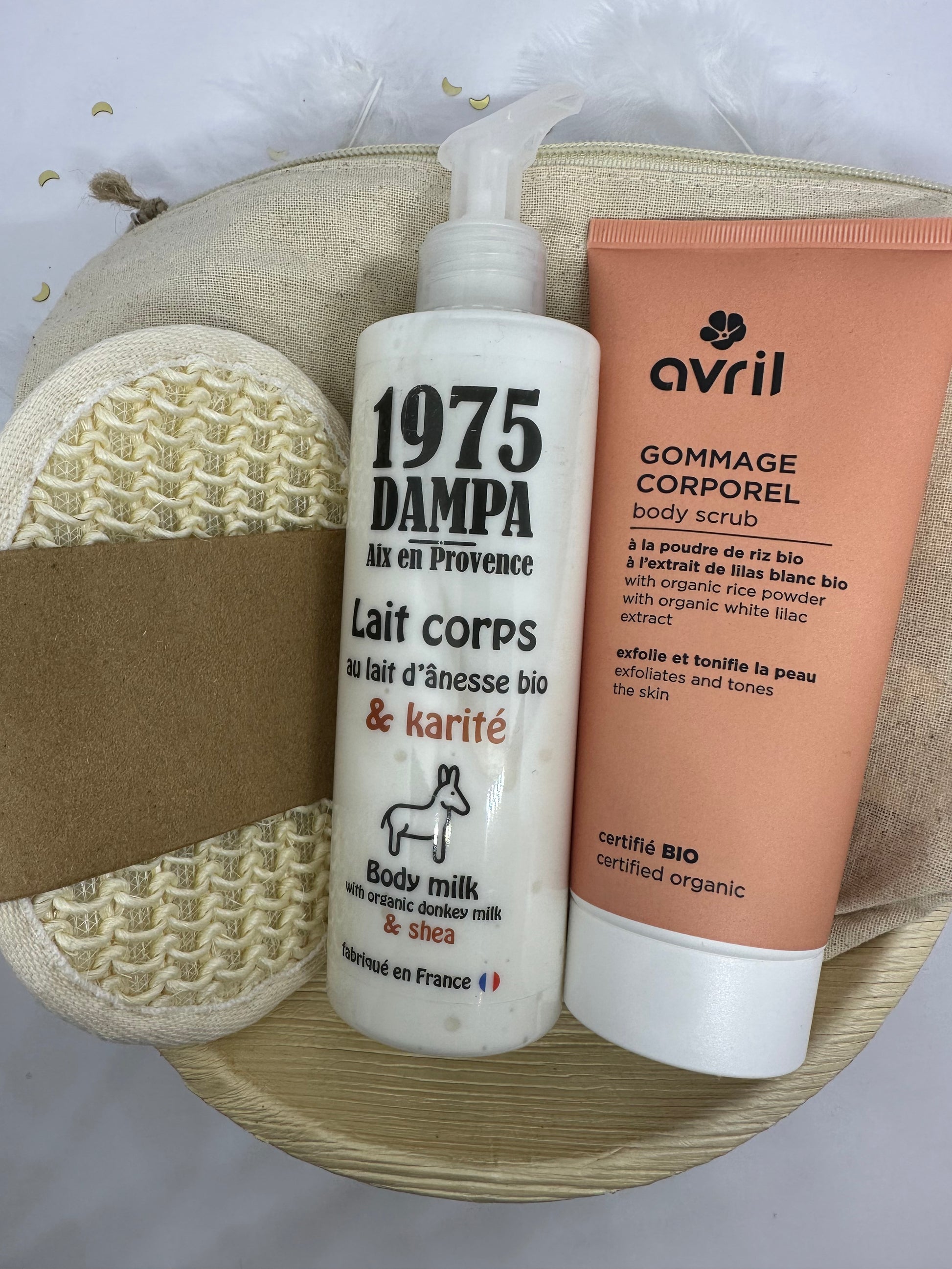 coffret avec plateau a la feuille d'areca, une éponge exfolliante écru en coton, un lait corps anesse et karité blanc, un gommage orange avril pour le corps et une trousse écru sur fond blanc avec paillettes dorées et plumes blanches