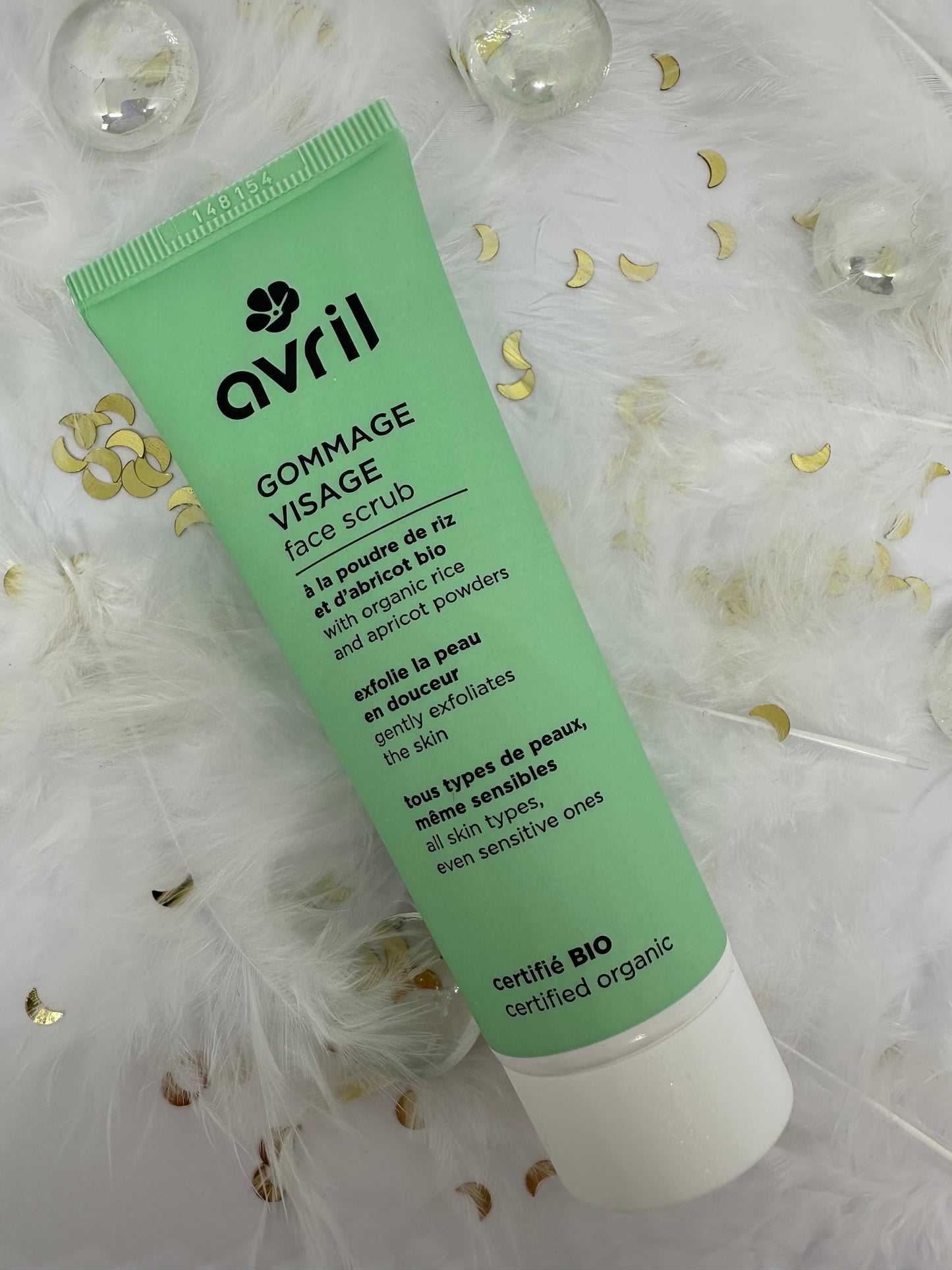 Gommage visage bio Avril sur décor blanc avec paillettes, plumes et billes transparentes - soin exfoliant du Coffret Teint Radieux