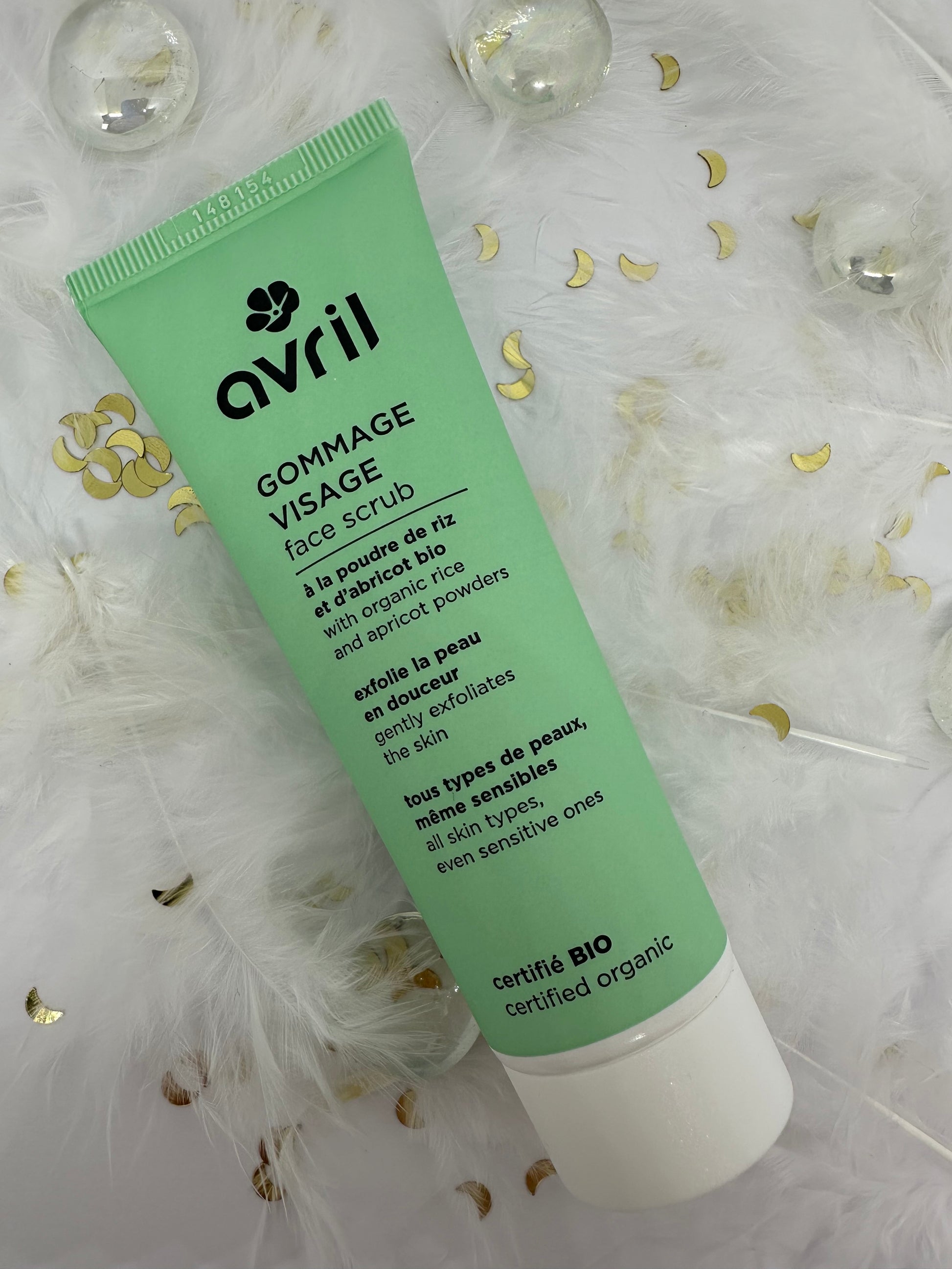 Gommage visage bio Avril sur décor blanc avec paillettes, plumes et billes transparentes - soin exfoliant du Coffret Teint Radieux
