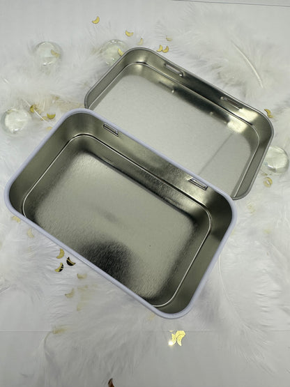 boite à savon métal blanc ouverte sur fond blanc avec plumes blanches, paillettes dorées et billes transparentes