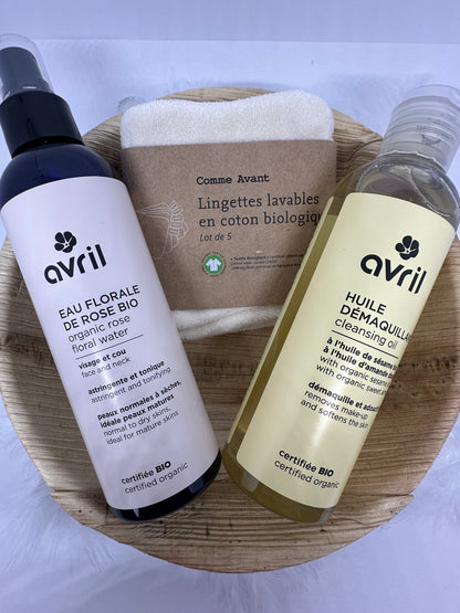 coffret douceur bio avec plateau en feuille d'areca, une eau florale de rose avril, une huile démaquillante avril et un lot de lingette bio en coton écru sur fond blanc et plumes blanches