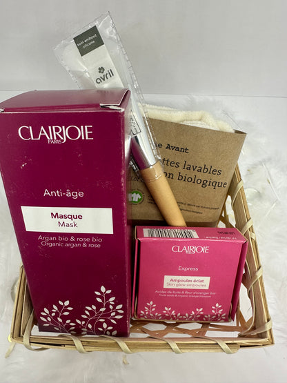 coffret rituel dans un panier en bambou couleur bois, un pinceau bout silicone manche en bois avril, un masque argan et rose clairjoie, une boite d'ampoules clairjoie et un lot de lingettes bio coton comme avant sur fond blanc et plumes blanches