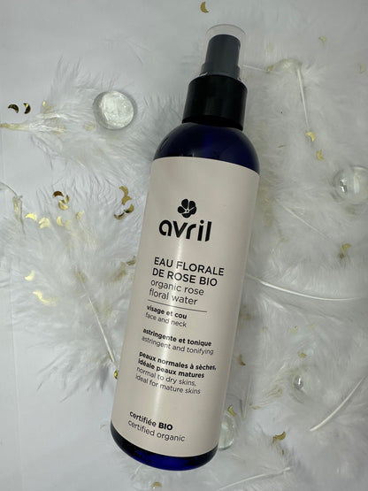 eau florale de rose bio avril sur fond blanc avec plumes blanches, billes transparentes et paillettes dorées