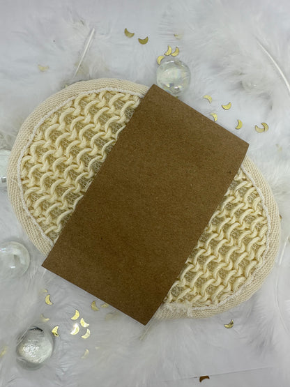 éponge exfolliante écru en coton sur fond blanc avec paillettes dorées, plumes blanches et billes transparentes