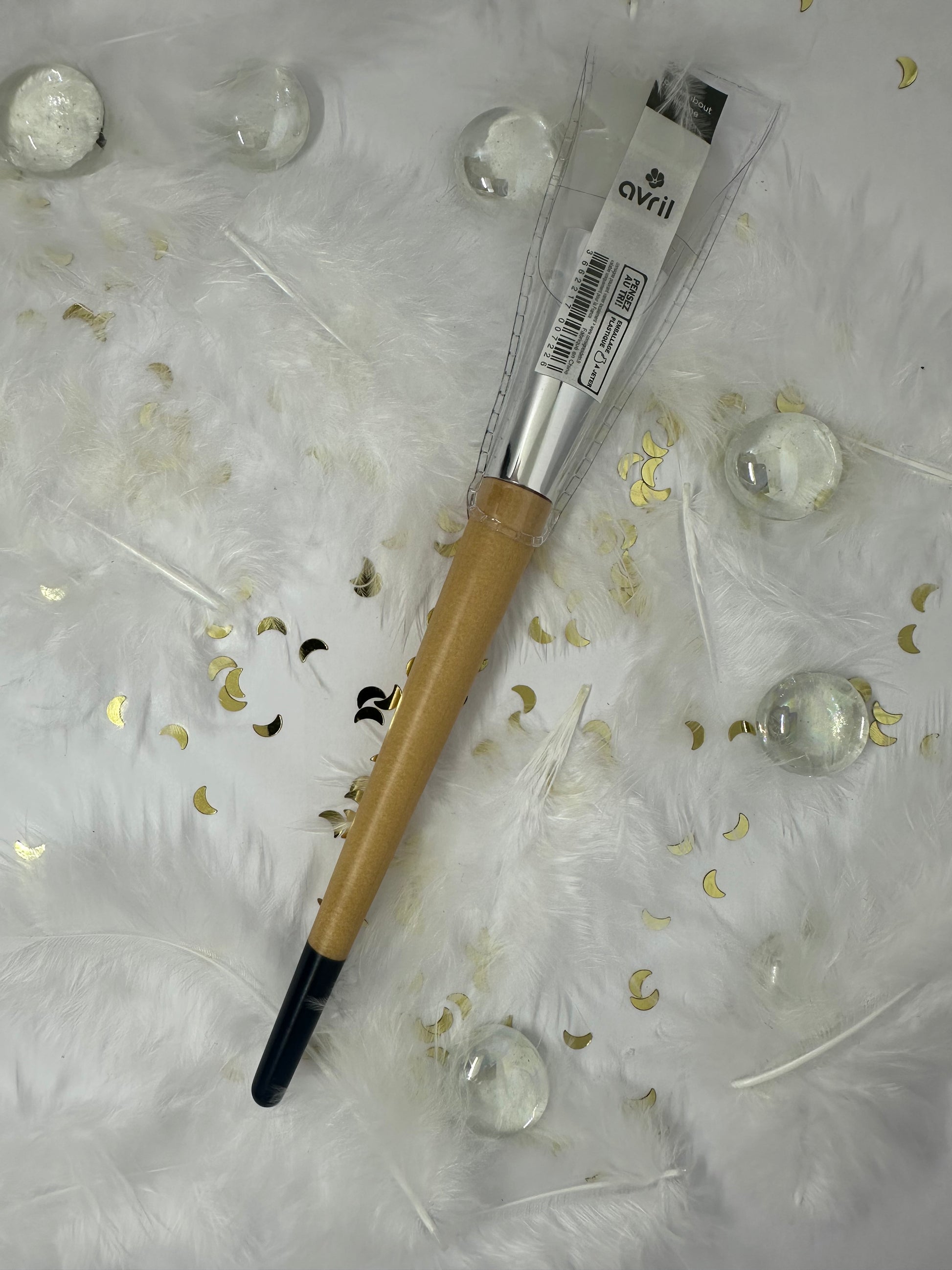 pinceau bout silicone blanc, manche bois bout noir sur fond blanc avec paillettes dorées, plumes blanches et billes transparentes